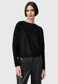Black, loose-fit sweater made of soft knit fabric with a wide neckline and long sleeves, paired with black, leather trousers.