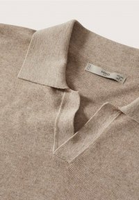 Polo beige en maille avec une texture douce, doté d'un col classique à rabat et d'une patte de boutonnage à trois boutons au niveau de l'encolure.