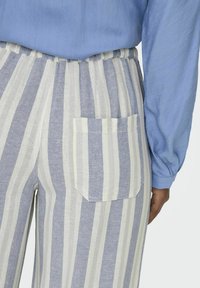 Lichtblauw overhemd met lange mouwen, gecombineerd met gestreepte linnen broeken in blauw en crème, met een achterzak en elastische tailleband.