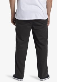 Pantaloni neri a vestibilità rilassata, realizzati in cotone, presentano una superficie liscia e sono abbinati a sneakers nere basse.