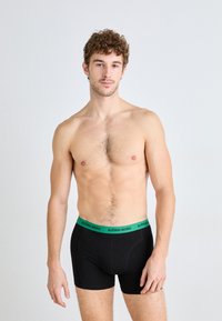Black boxer briefs with a green "BJÖRN BORG" waistband. Fabric appears smooth and fitted, showcasing a contemporary design.