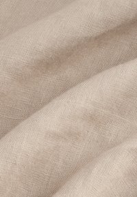 Hellbeiges Leinengewebe mit einer strukturierten Webart, das glatte, fließende Falten und subtile Tonvariationen zeigt.
