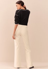 Maglione nero con cuciture a contrasto bianche, abbinato a pantaloni a zampa color crema. L'outfit presenta una vestibilità rilassata e una texture liscia.