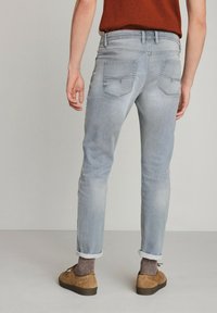 Vaqueros ajustados de color gris claro con un aspecto desgastado, que cuentan con dos bolsillos traseros y dobladillos enrollados, combinados con zapatos marrones y calcetines texturizados.