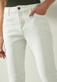 Bílé džíny z denimu s úzkým střihem, předními kapsami a kovovým knoflíkem na pásku, s hladkým povrchem.