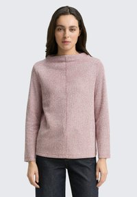 Langärmliger Pullover mit Rundhalsausschnitt aus leicht rosa-weiß meliertem Strick. Hat eine lockere Passform und subtile Nahtdetails. Getragen mit dunklen Jeans.