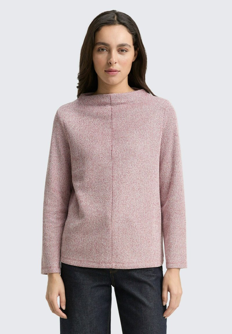 Langärmliger Pullover mit Rundhalsausschnitt aus leicht rosa-weiß meliertem Strick. Hat eine lockere Passform und subtile Nahtdetails. Getragen mit dunklen Jeans.