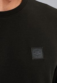 Schwarzer, strukturierten Sweatshirt mit Rundhalsausschnitt und quadratischem Logo-Patch auf der linken Brust mit geprägten Details.