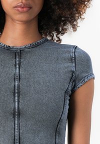 Siva denim majica s kratkimi rokavi, ki ima okrogel izrez in vidne šive ob šivih, kar ustvarja teksturiran videz.