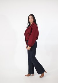 Bordowa krótka kurtka z podwójnym rzędem guzików, zestawiona z ciemnymi dzwonami z denimu i karmelowymi szpilkami. Gładka tkanina z bufkami na rękawach.