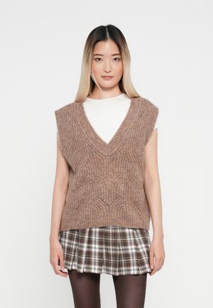 Knit, sleeveless vest in light brown with a V-neck and textured pattern. Paired with a plaid mini skirt in brown, white, and black.