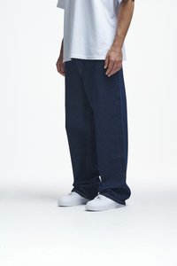Dunkelblaue weitem Beinen Denim-Jeans mit orangefarbenen Nähten. Getragen mit einem lockeren weißen Baumwoll-T-Shirt und weißen Sneakern.