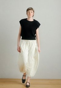 Μαύρο πλεκτό τοπ με φαρδιά μανίκια, σε συνδυασμό με λευκά παντελόνια με πουά πουά, δεμένα στη μέση. Το μοντέλο φοράει μαύρα επίπεδα παπούτσια.