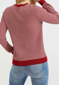 Pull rouge et blanc à motif avec un col rond et des poignets côtelés, présentant un design en tricot texturé et une silhouette ajustée.