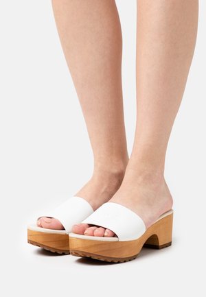 Białe skórzane sandały na obcasie z szerokim paskiem i otwartym przodem. Posiadają naturalny, drewniany obcas blokowy z teksturowaną podeszwą dla lepszej przyczepności.
