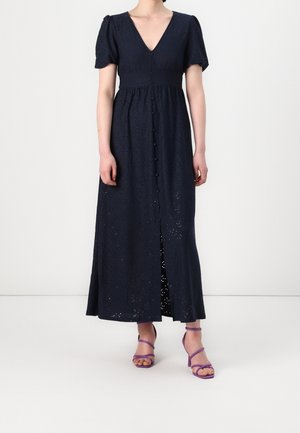 Granatowa sukienka do kostek z krótkimi bufkami, guzikami z przodu, dekoltem w serek i fioletowymi sandałami na obcasie z paskami.