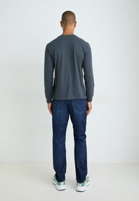 Camiseta gris de manga larga con escote redondo, combinada con pantalones vaqueros azul oscuro. Zapatillas blancas con detalles verdes completan el conjunto.