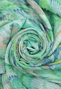 Sciarpa leggera e stampata in tonalità di verde con motivi floreali astratti. Tessuto morbido e fluido, arrotolata ordinatamente in una forma a spirale.