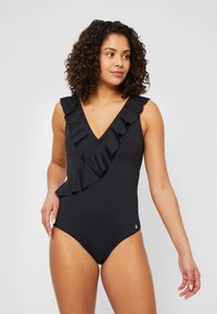 Maillot de bain une pièce noir avec un décolleté en V plongeant et un accent volanté sur le côté gauche. Fabriqué en tissu lisse et extensible.