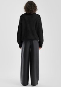 Zwarte gebreide trui met hoog col en oversized pasvorm, gecombineerd met zwart leren wijde broek met hoge taille. Gestructureerd, casual ontwerp.