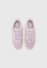 Une paire de baskets Nike Air roses avec des lacets, une boîte à orteils perforée et des semelles blanches placées côte à côte sur un fond blanc.