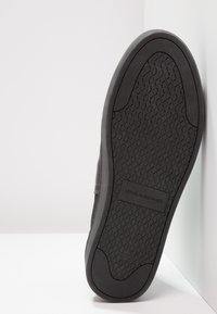 La suela de goma negra presenta un patrón de agarre texturizado y un logo de "VAGABOND". El borde es redondeado y liso, con un diseño minimalista.