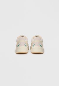 Beige sneakers with thick off-white soles, green and blue accents, shown from the back on a plain light gray background.