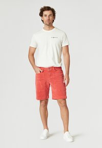 Röda radarshorts med två framfickor och knappstängning. Matchas med en vit t-shirt med kort ärm som har en svart logotyp. Vita sneakers.