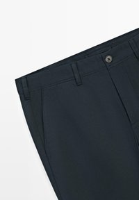 Pantaloni sartoriali blu scuro con chiusura a bottone, passanti per cintura e tasche laterali, mostrati distesi su uno sfondo bianco.