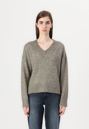 Gray, V-neck sweater made of soft fabric with a loose fit and ribbed hem. Worn with dark denim jeans. Simple design, no visible patterns.