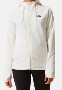 Giacca in pile bianca con zip e cappuccio, dotata di un logo nero sul petto, tasche laterali e polsini con foro per il pollice per un maggiore calore.