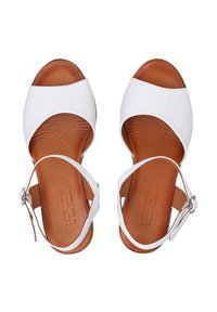Sandales blanches en cuir avec une large sangle à l'avant du pied et une sangle de cheville ajustable, dotées d'une semelle intérieure en cuir brun, d'une texture lisse et d'une boucle ronde.