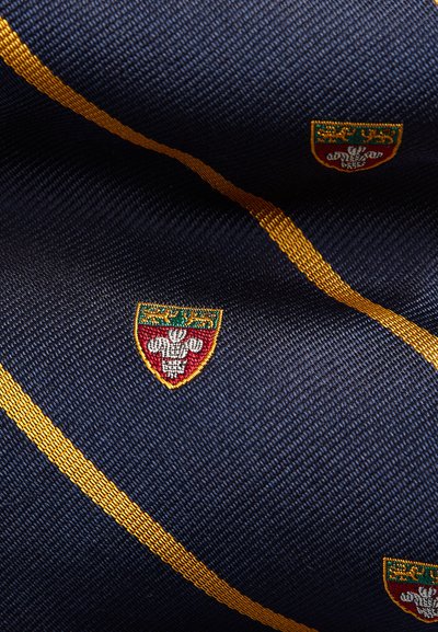 Tessuto blu navy con una texture sottile, caratterizzato da strisce diagonali dorate e stemmi ricamati in colori a contrasto.