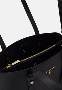 Mustangin musta nahkalaukku kultaisilla yksityiskohdilla, jossa on vetoketjullinen osasto ja sileä pinta. Sisäosassa on brändin kultainen nimilaatta.