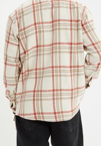 Camisa de manga larga a cuadros en color crema, con cuadros rojos y beige, textura suave y un corte relajado con bajo redondeado y puños con botones.