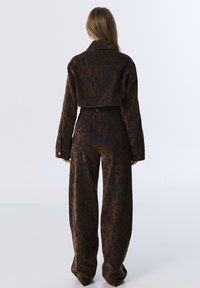 Cropped jacket and wide-leg pants in textured brown and navy fabric with a floral pattern. Features button detailing and long sleeves.