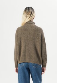 Maglione marrone a coste con collo alto, caratterizzato da spalle scese e vestibilità ampia, abbinato a jeans blu a vita alta.