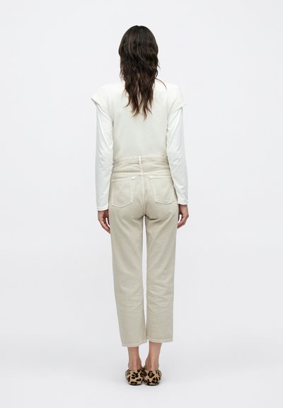 Μπεζ ψηλόμεσο παντελόνι με ίσια παντελόνα και πίσω τσέπες, συνδυασμένο με εφαρμοστό κρεμ τοπ και slip-on παπούτσια με μοτίβο λεοπάρ.