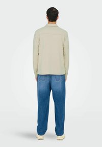 Light beige long-sleeve shirt with a collar and back yoke, paired with loose-fitting blue jeans featuring back pockets and a faded texture.