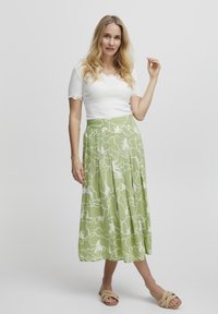 Roheline plisseeritud seelik valgete abstraktsete mustritega; valmistatud kergest kangast. Kombineeritud istuva valge pluusi ja beežide sandaalidega.