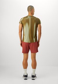 Herretrimmet atletisk skjorte i olivengrønn med vertikale striper, parret med maroon shorts. Skjorten har et teksturert, lett materiale.