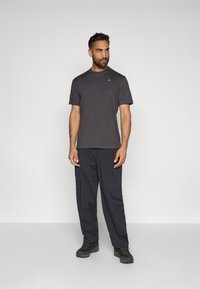 T-shirt preta de gola redonda com mangas curtas, apresentando um pequeno logótipo azul. Combinada com calças cargo pretas e calçado escuro.