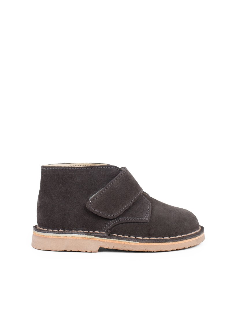 Stivale alla caviglia in suede grigio con una larga fascia in velcro, cuciture beige e una suola in gomma marrone chiaro a contrasto. Design compatto e arrotondato.