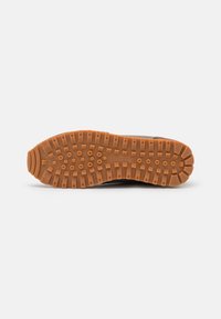 Schuhsohle mit erhöhten quadratischen und runden Profilen in einem symmetrischen Muster, aus Gummi, vor einem schlichten weißen Hintergrund präsentiert.