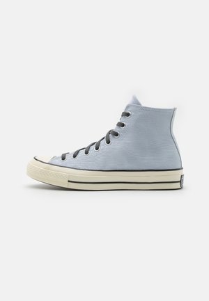Baskets montantes en toile bleu clair avec lacets noirs, semelle en caoutchouc blanche et bande noire le long du bord de la semelle, vues de côté.