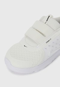 White athletic shoe featuring mesh and synthetic fabric with two Velcro straps, Nike branding, textured sole, and a rounded toe design.