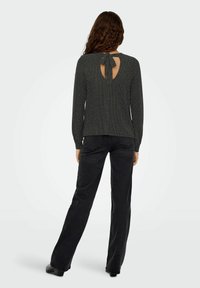 Donkergrijze gebreide trui met lange mouwen en een striksluiting aan de achterkant. Draagt bijpassende zwarte uitlopende jeans en enkellaarzen.