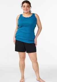 Türkisfarbenes geripptes Tanktop mit gezacktem Ausschnitt und schwarzen Shorts. Das Tanktop hat dünne Träger und einen abgerundeten Saum. Der Stoff wirkt weich und angenehm.