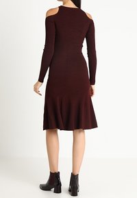 Vestido de punto acanalado burdeos con diseño off-the-shoulder, dobladillo acampanado y mangas largas. Combinado con botas negras hasta el tobillo.
