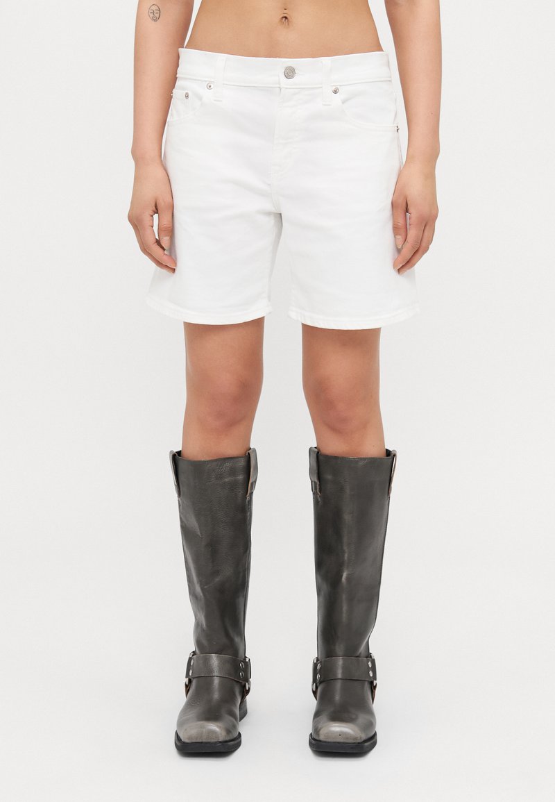 Pantalones cortos de mezclilla blanca con un ajuste regular, dobladillo vuelto, diseño de cinco bolsillos y herrajes en tono plateado, combinados con botas altas de cuero gris.